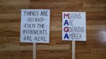 Two protest signs that say, "Things are so bad even the introverts are here" and " Morons Are Governing America."